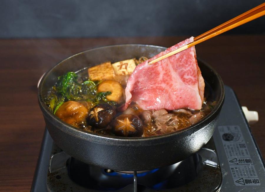 Chopsticks lifting a slice of marbled wagyu from a bubbling sukiyaki pot