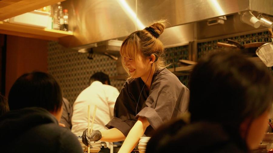 Smiling Chikarayama staff member cooking sukiyaki for guests at the counter